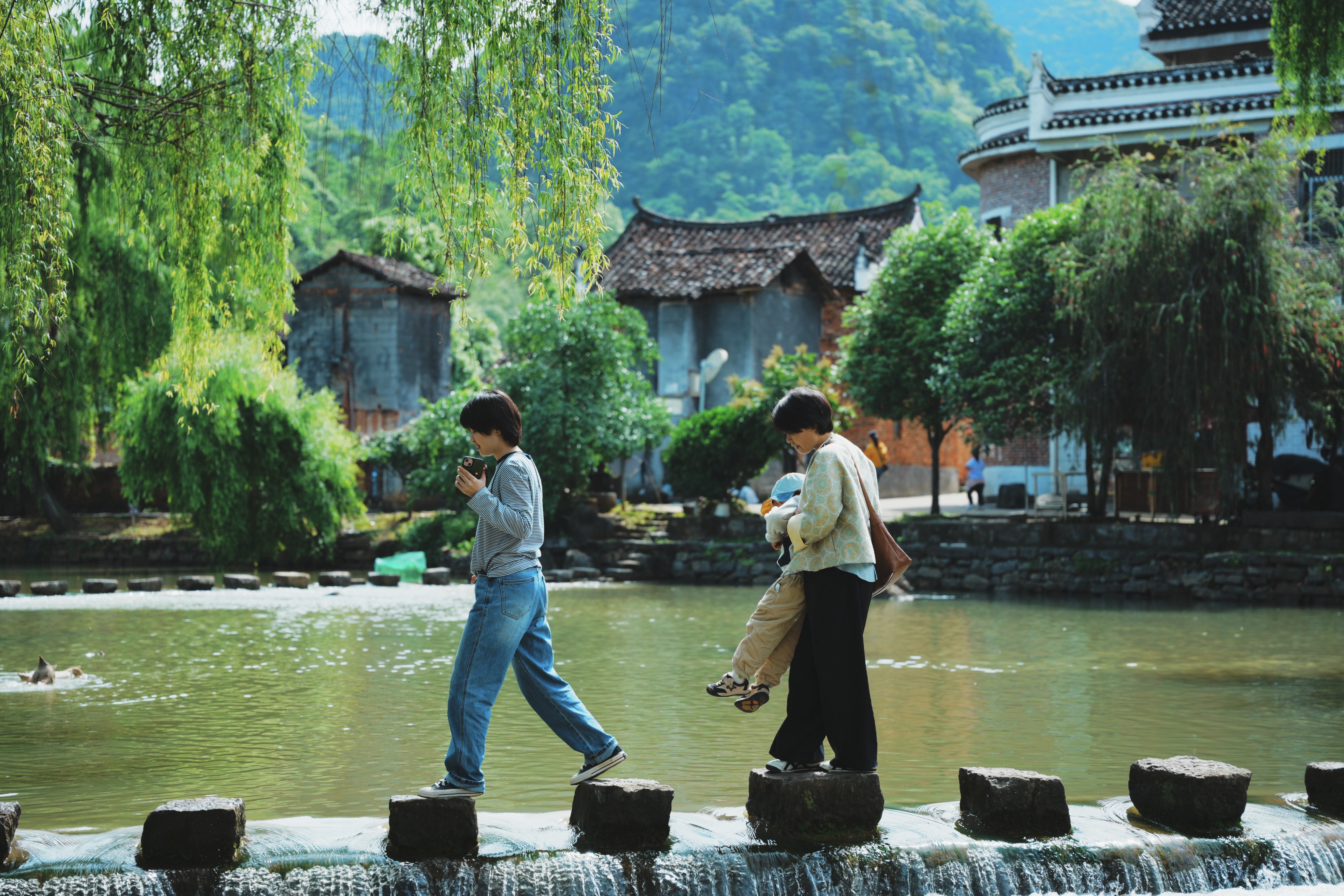 two people crossing a stone bridge across a pond