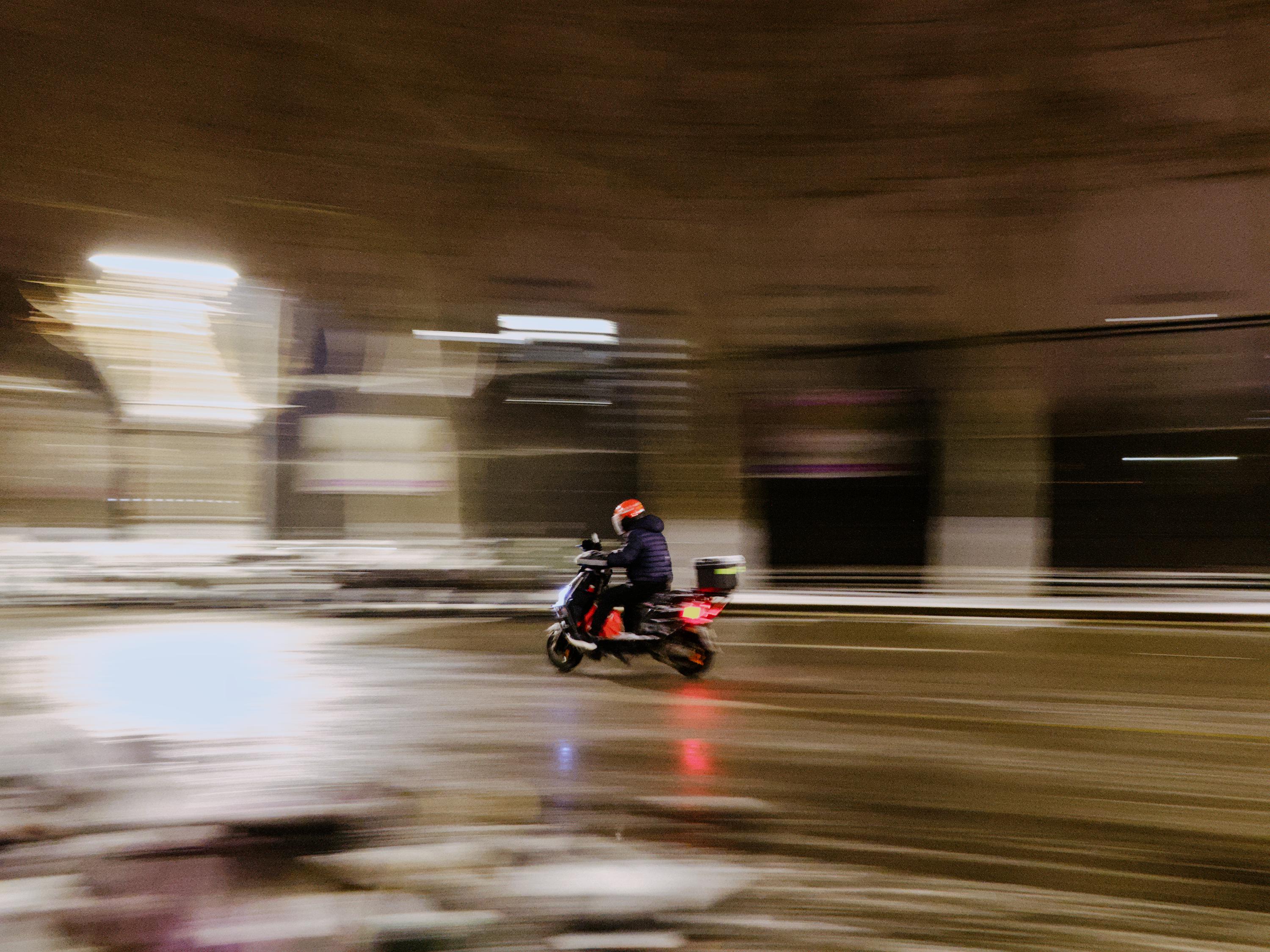 person on electric motorcycle driving left on road, surroundings are smeared out