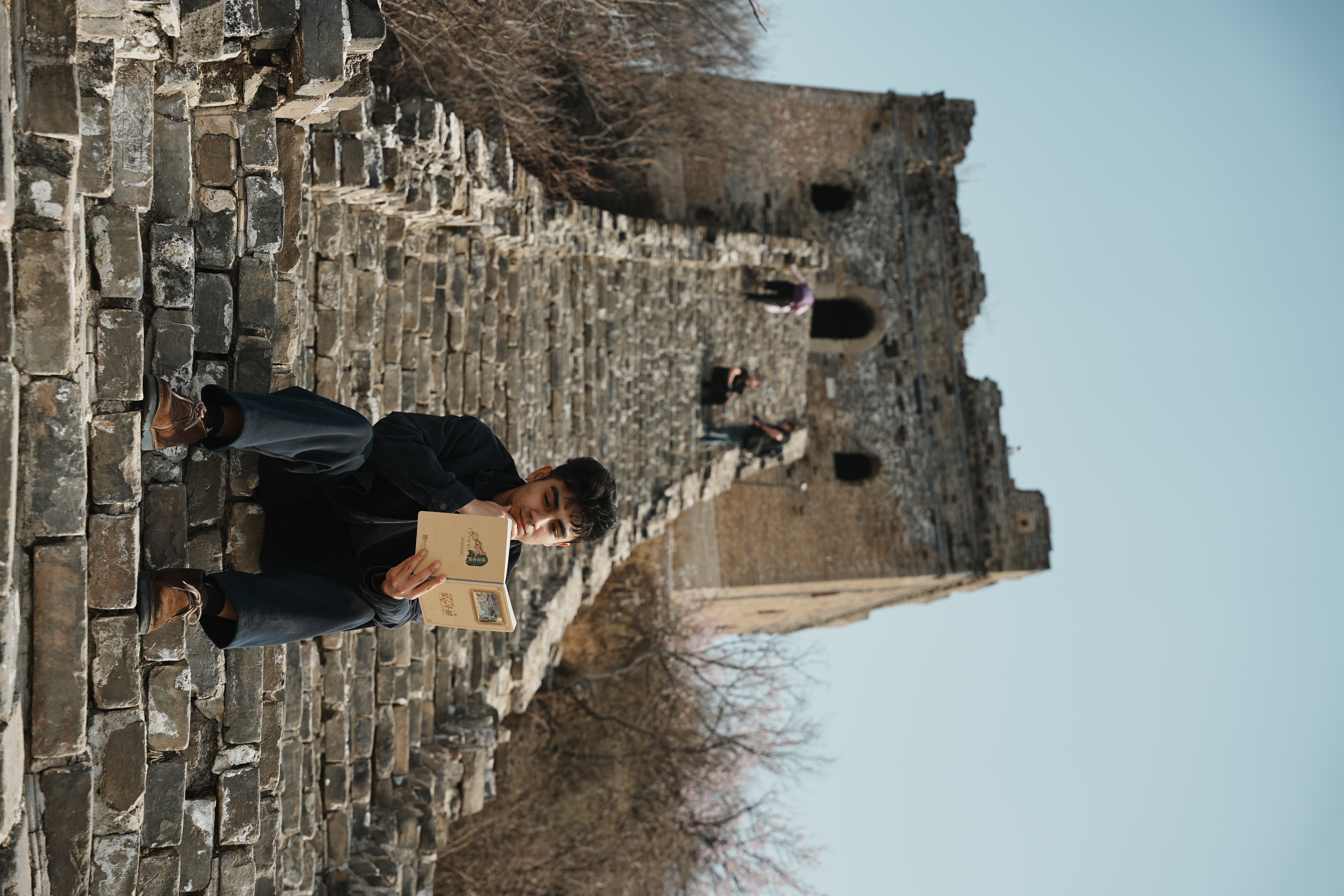 man sitting on the steps of the great wall of china and reading with a rampart as background