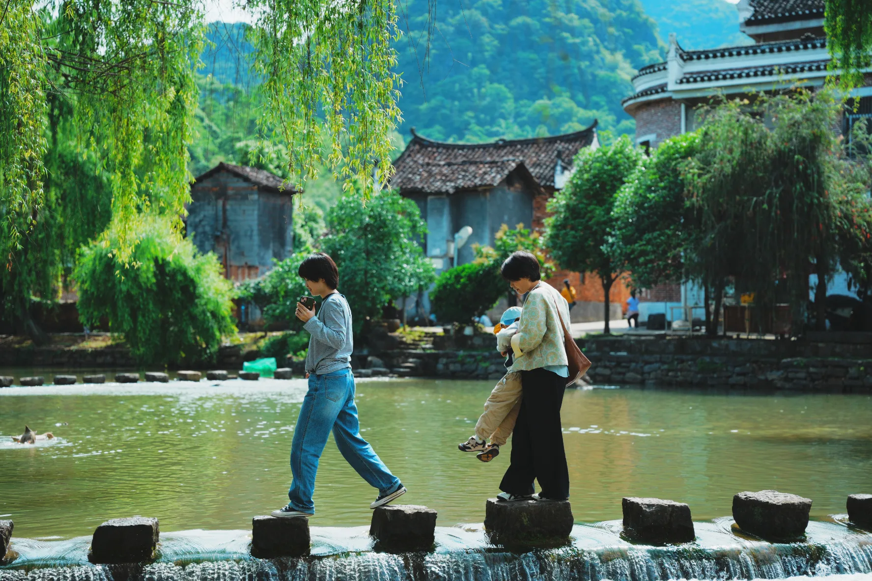two people crossing a stone bridge across a pond