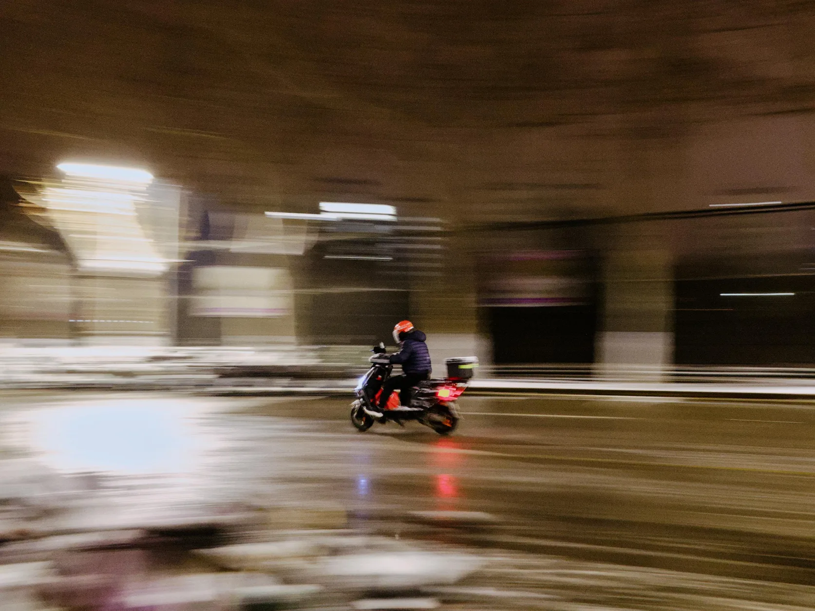 person on electric motorcycle driving left on road, surroundings are smeared out