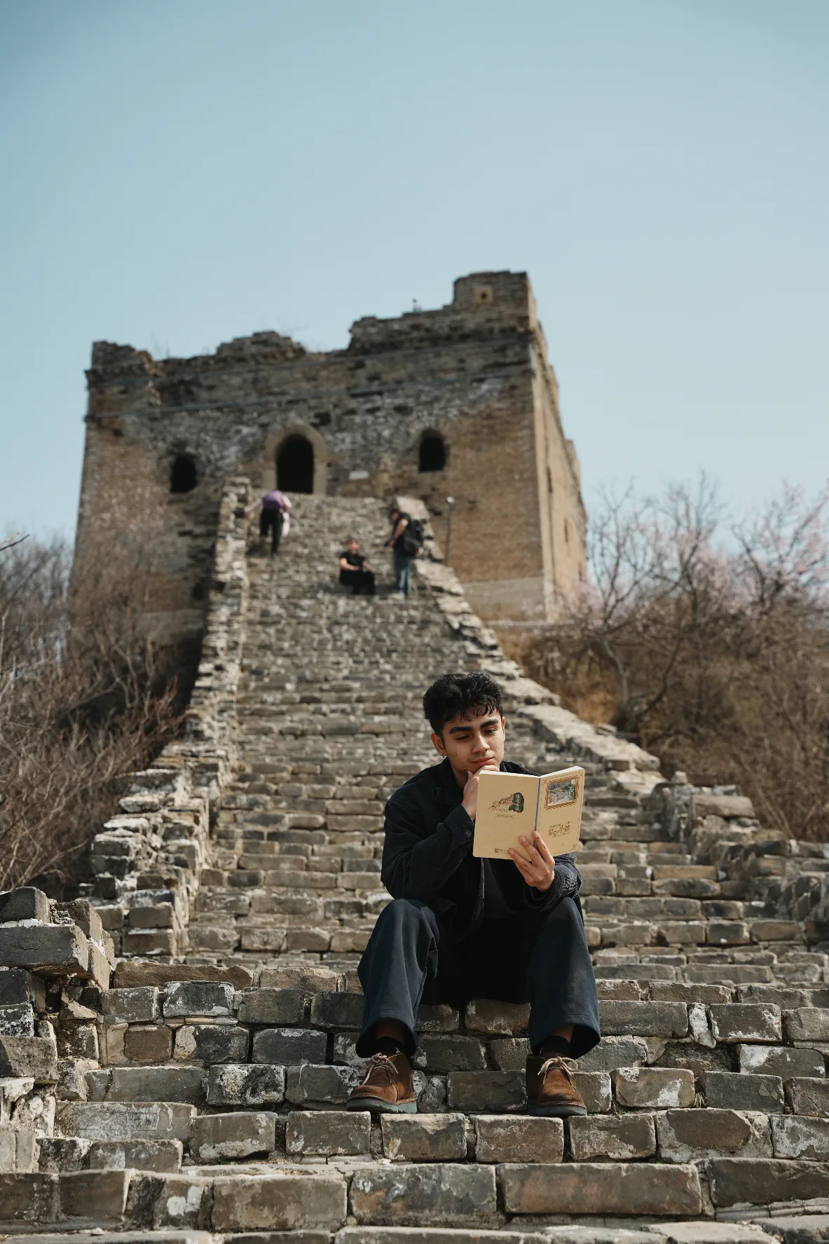 man reading a book against a rampart at the great wall of china